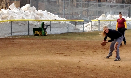 Cobber third baseman Paige Beseman fields a ground ball in the shadows of a giant snow pile.