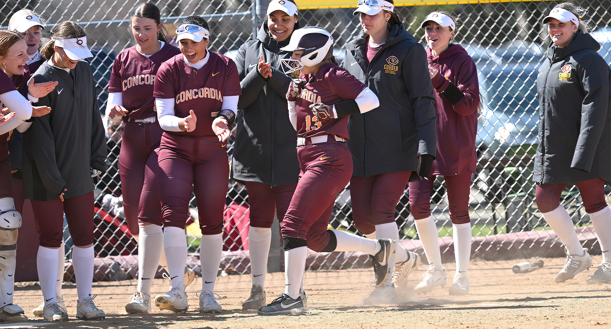 Cobber players wait to celebrate at home plate after Kailee Falconer (#13) hit her first collegiate homer in the second game against Bethel.