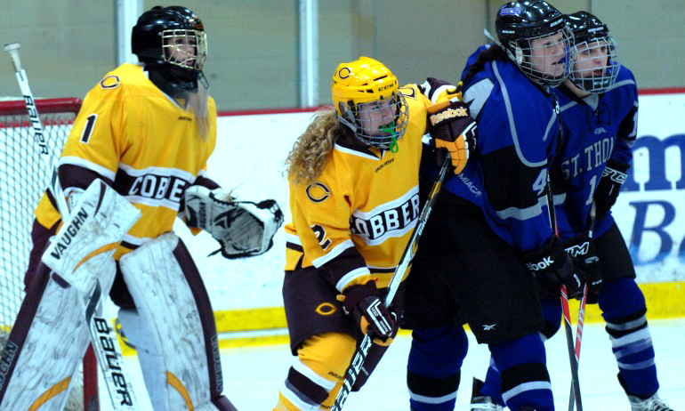Cobber junior defenseman Cassey Petrich tries to clear out a pair of Tommie forwards in front of goalie Andrea Klug.
